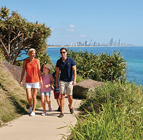 Two adults and a child walking on path with Gold Coast skyline in background