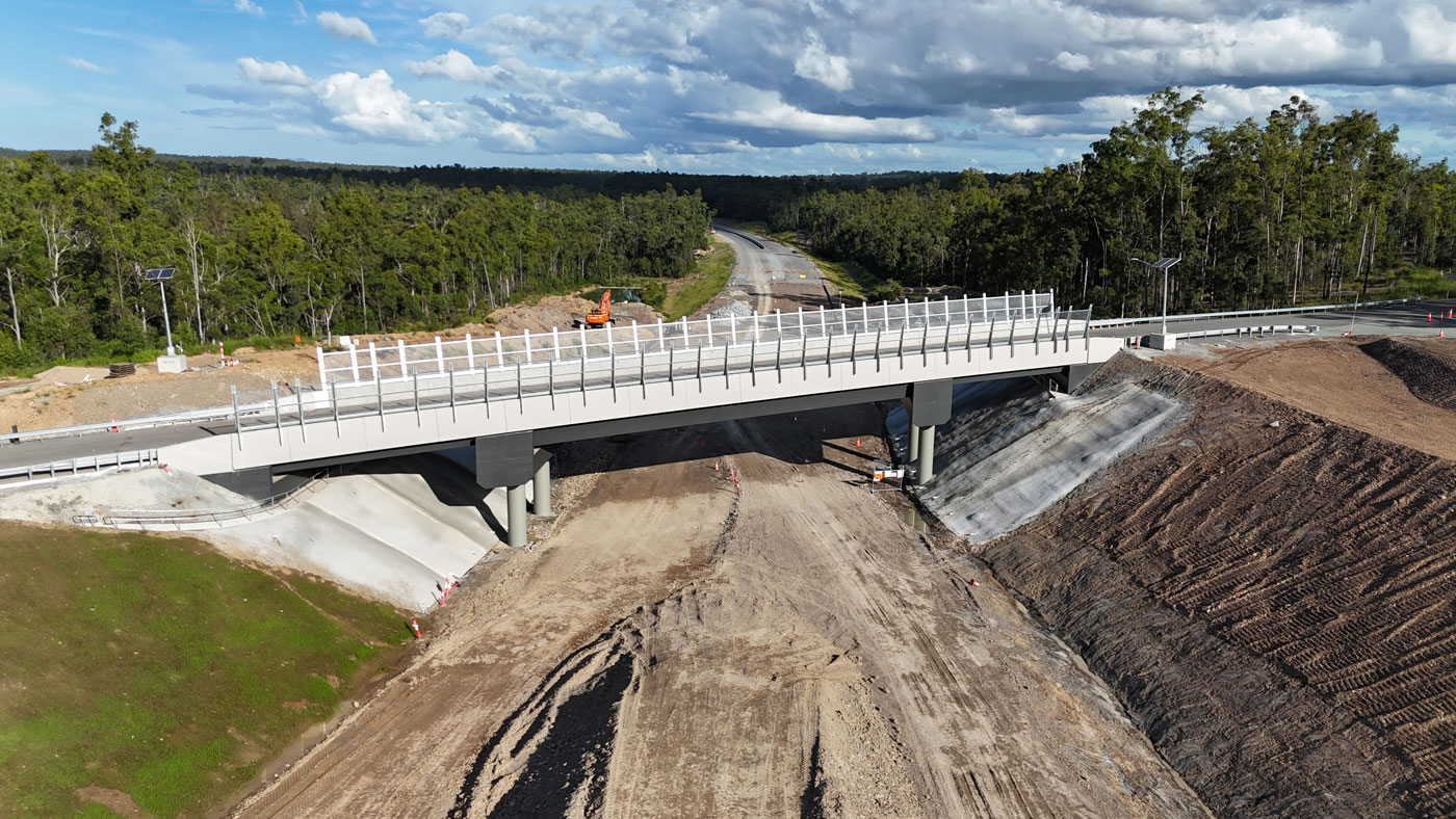 A close shot of the new bridge that carries Bolcaro Road over the new highway, the anti-throw screens are attached to the overpass bridge which stop commuters throwing things onto the new highway below once complete. The new highway has some earthworks in the foreground that are still underway (no pavement). Image is looking south through the Curra State Forest where the pavement begins for the new highway.