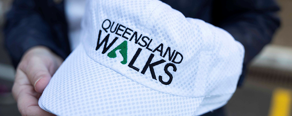 Person holding a white hat with Queensland Walks logo