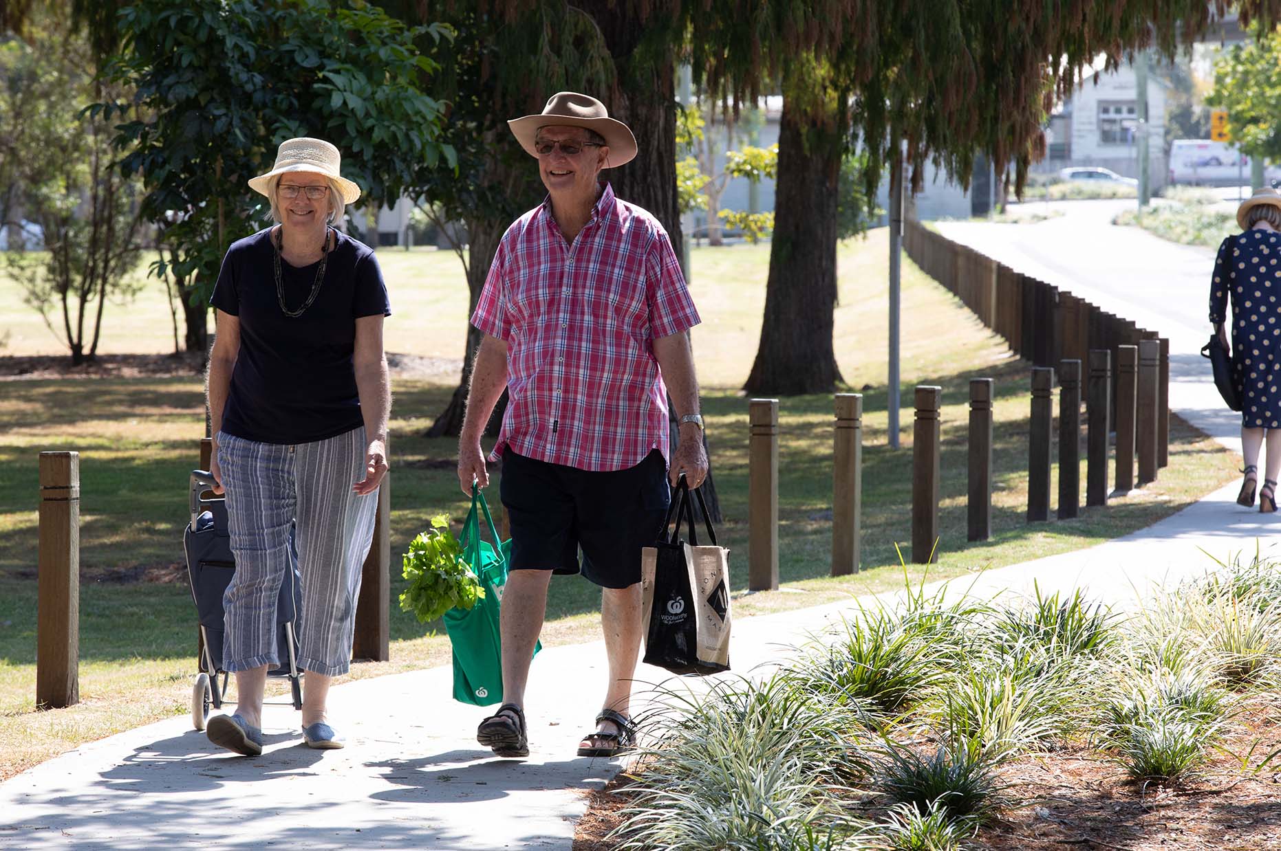 An elderly couple walking down a path carrying shopping bags