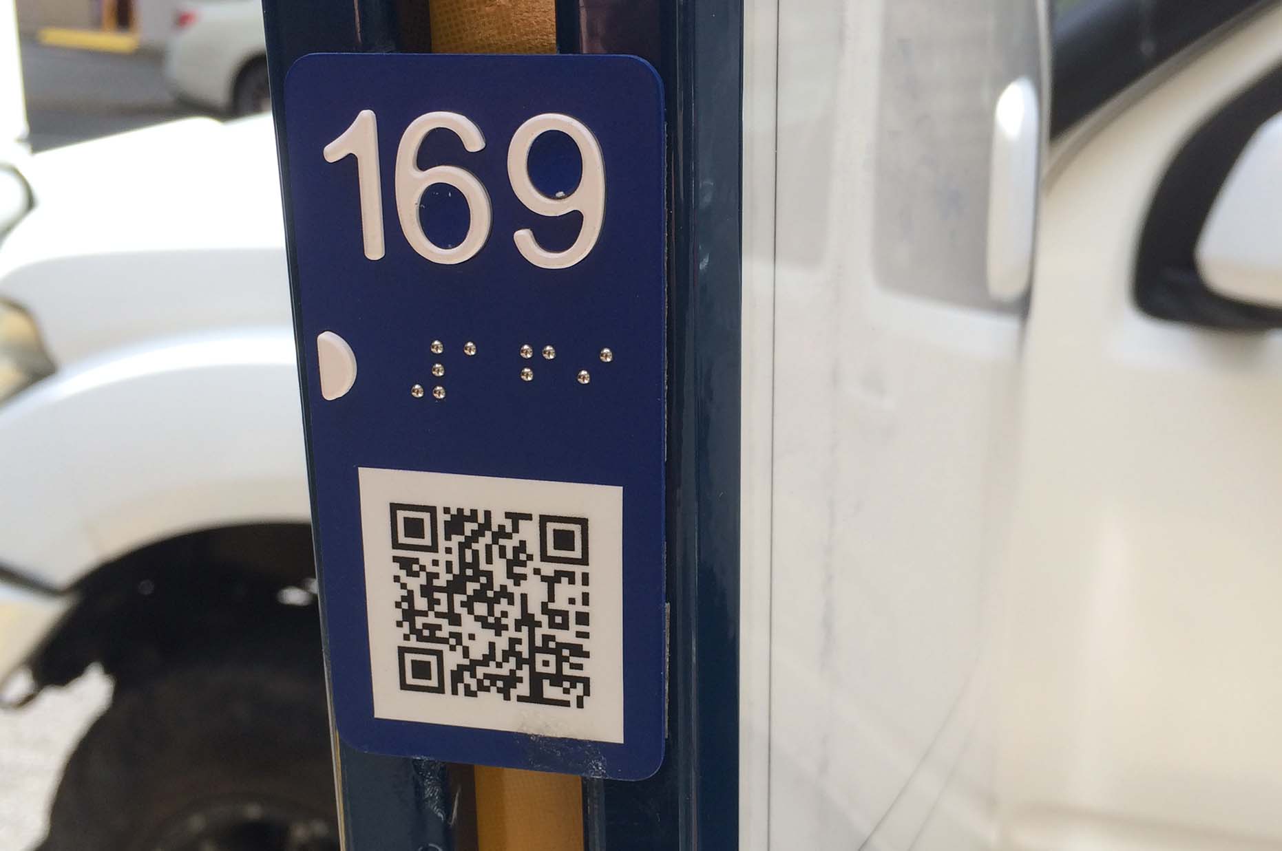 Bus stop with 169 written numbers and in braille, also displaying a QR code 
